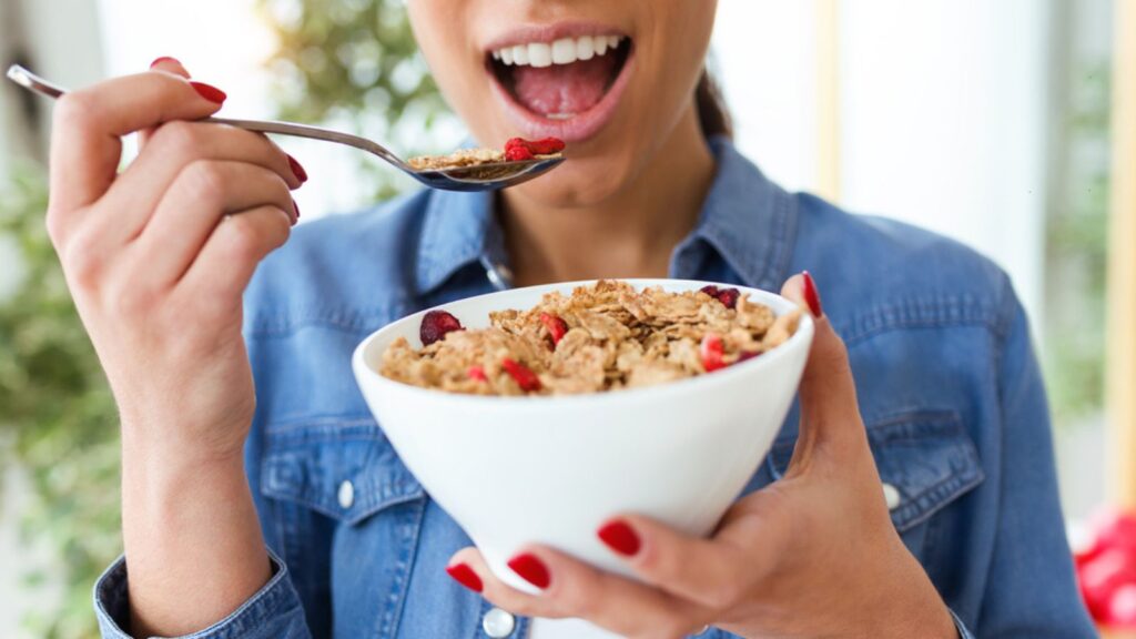 Close-up of smiling young woman eating breakfast cereals of bowl at home