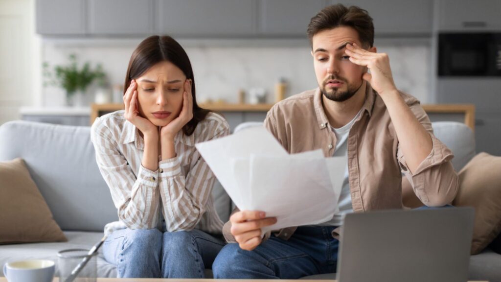 Concerned young couple examining financial documents debt budget worried sad