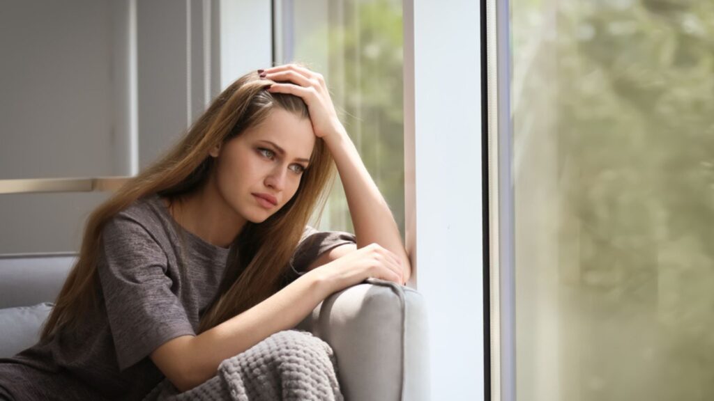 Depressed thinking sad young woman sitting on sofa at home