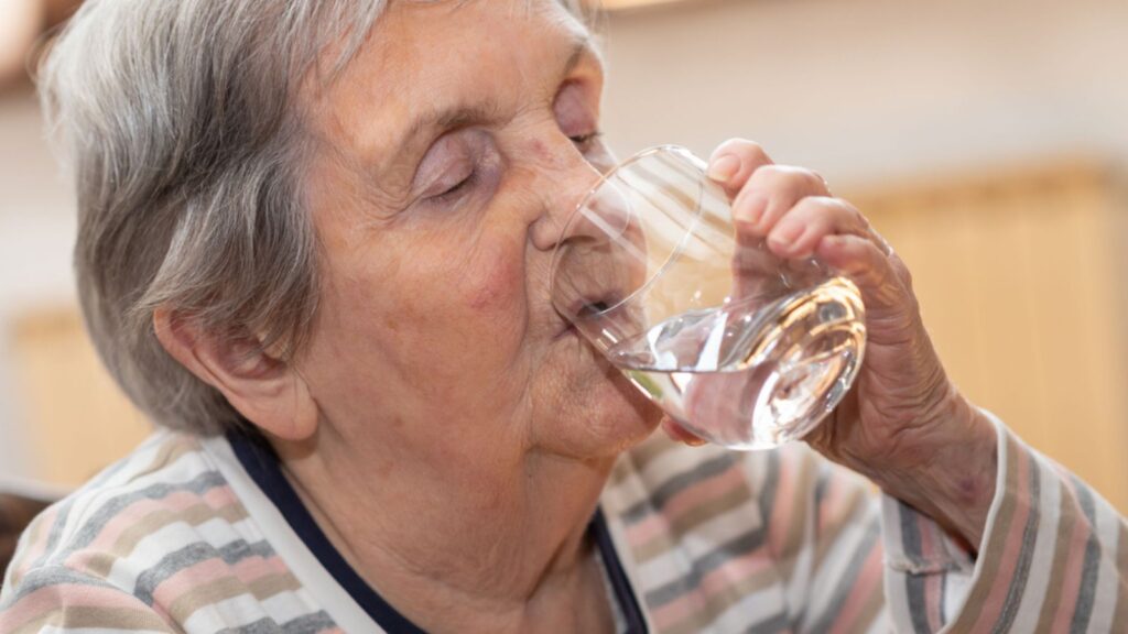 Elderly woman drinking water at home