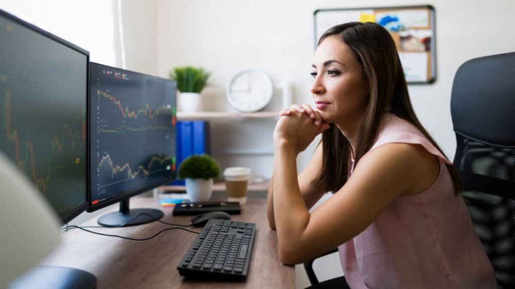 Freelance young woman working as a broker at home and looking at the computer monitor while checking the stock market