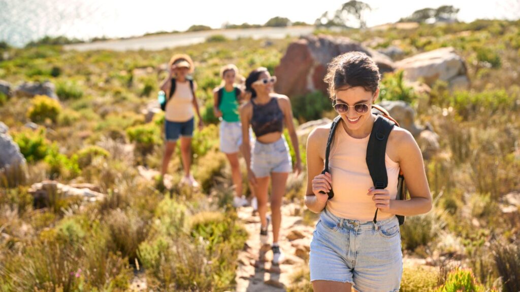 Group Of Friends woman With Backpacks On Vacation On Hike Through Countryside Next To Sea