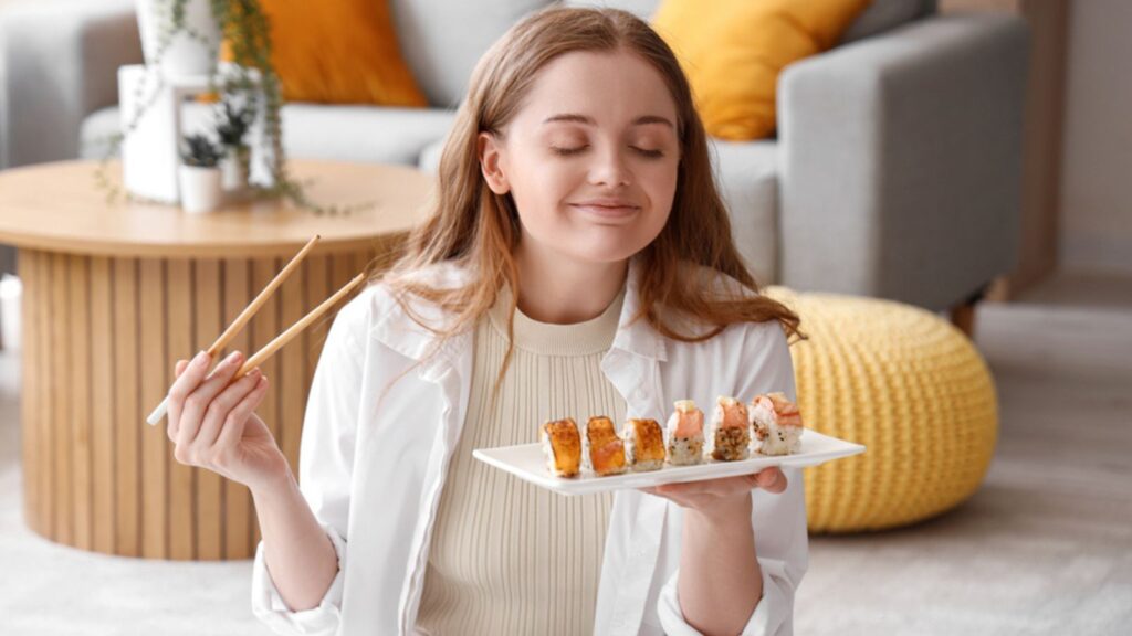 Happy young woman eating sushi in living room