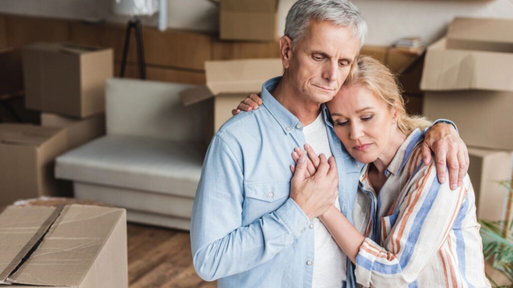 High angle view of upset senior couple embracing and holding hands during house relocation