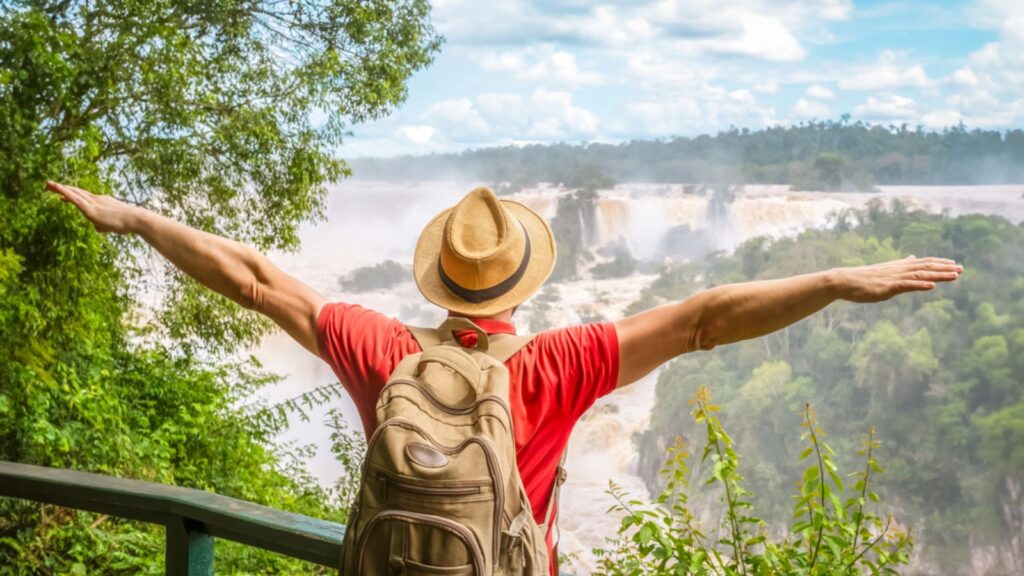 Iguazu Waterfalls, Brazil - Traveler man with raised arms watching Iguacu Falls in Brasil and Argentina.