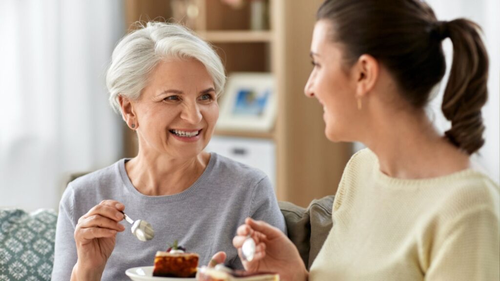 Old mother and adult daughter eating cake at home