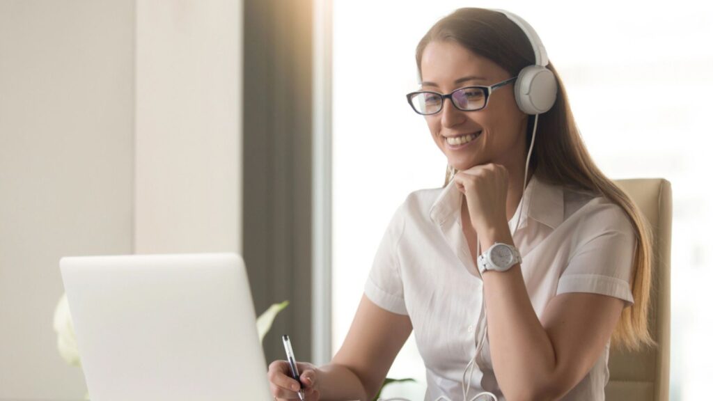 Smiling young businesswoman wearing headphones working freelance on laptop