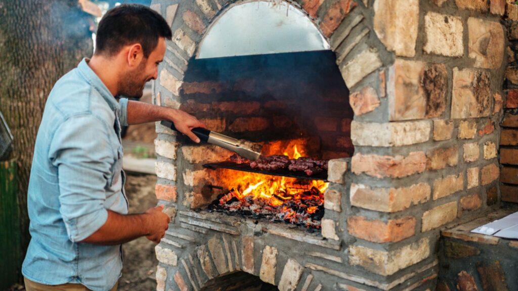 Summertime fun. Young man cooking meat on a brick barbecue.