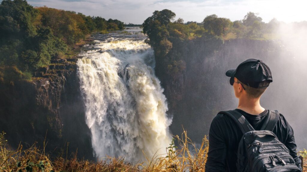 Tourist man looks at the Victoria Falls on Zambezi River in Zimbabwe