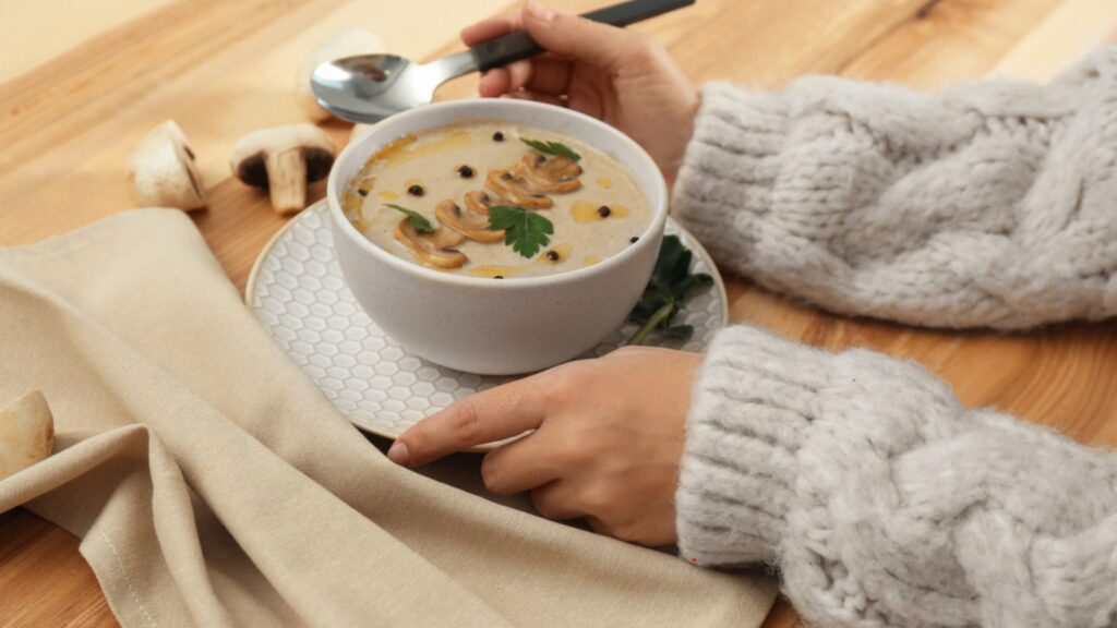 Woman eating with fresh mushroom soup at wooden table, closeup