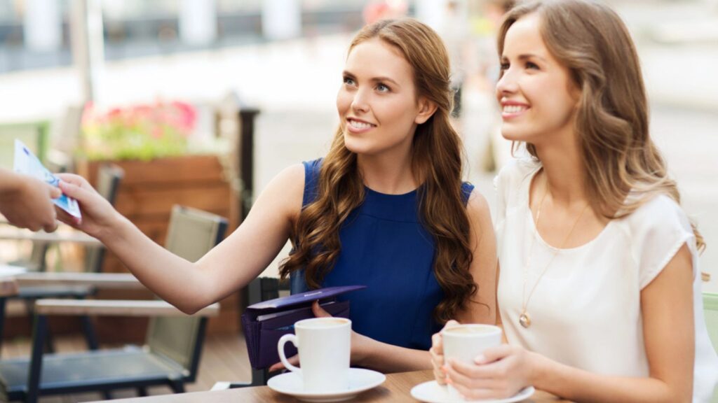 Women paying money to waiter for coffee at cafe