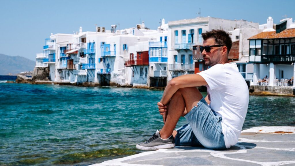 Young man on vacation at the Greek Island of Mykonos, men relaxing at the little venice village of Mykonos Island