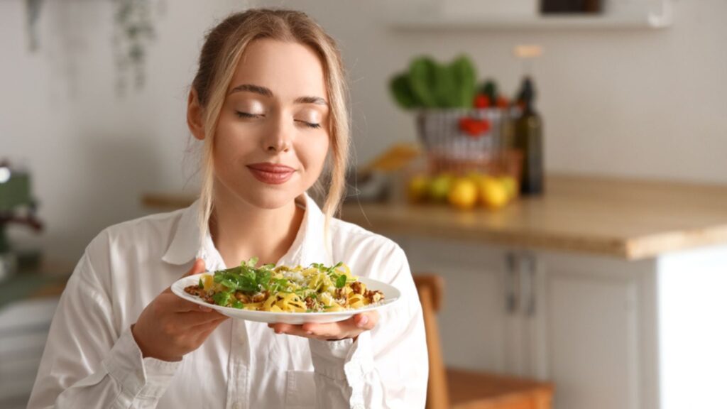 Young woman smelling the tasty pasta in kitchen