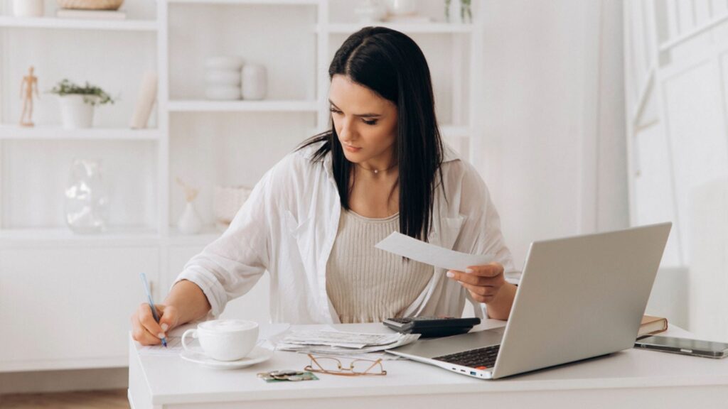 focused woman doing taxes bills on laptop and drinking coffee