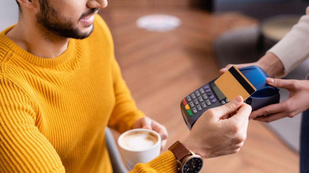 man in yellow sweater at coffee shop paying cashier with credit card