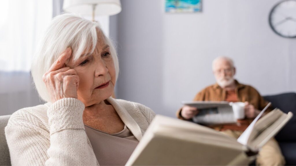 old man sitting behind stressed woman reading book in living room
