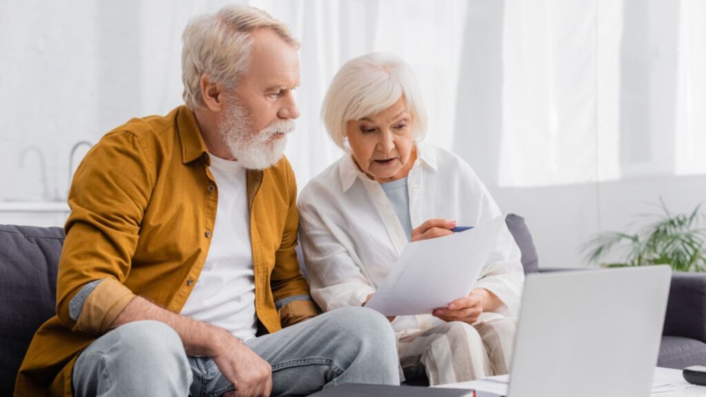 senior retired old elderly couple planning budget finances on couch with laptop