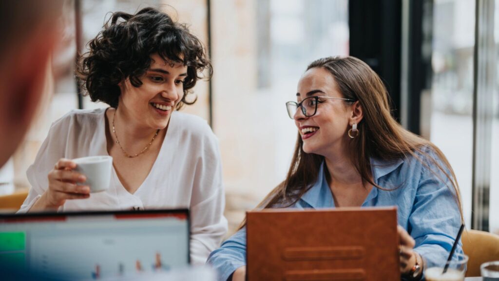 two happy professional women talking and drinking coffee at work