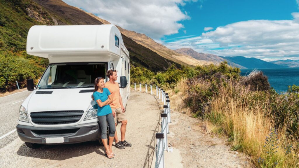 young travel tourist couple standing against motorhome RV on coastal road