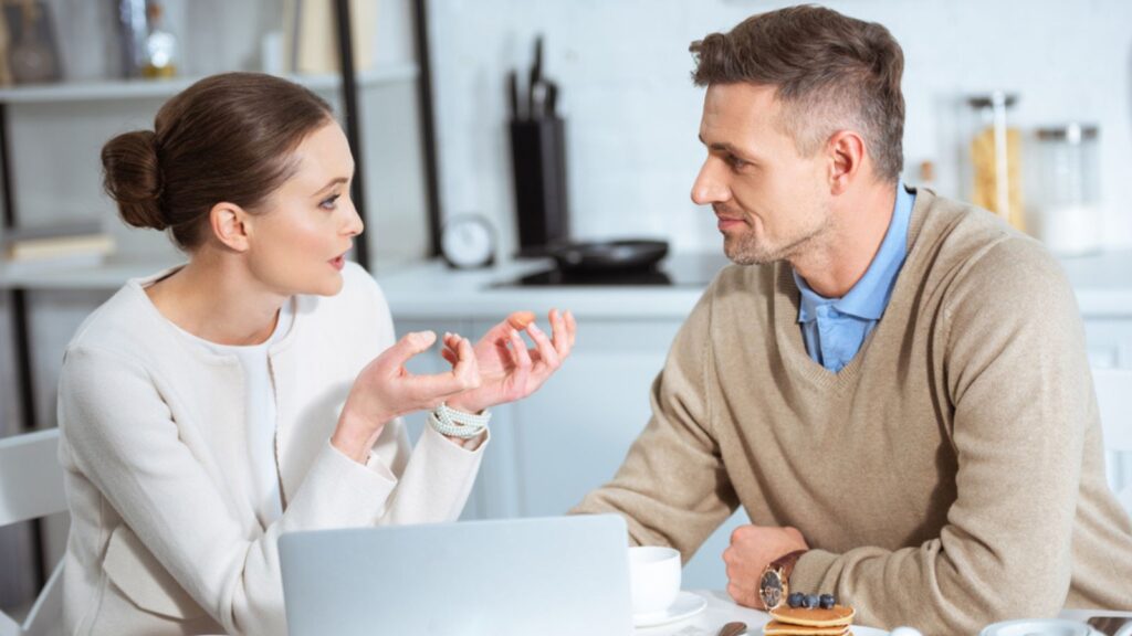 Adult couple using laptop and having conversation during breakfast in morning