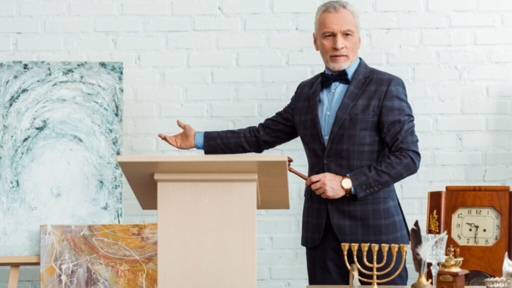 Auctioneer holding gavel and pointing with hand at picture during auction