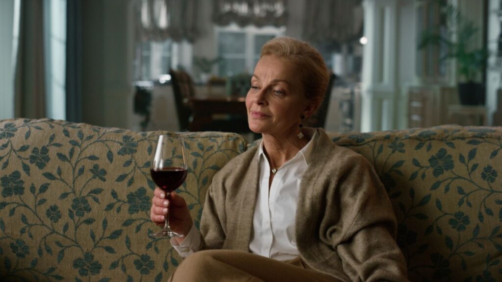 Dreamy mature woman tasting red wine glass in vintage living room. Senior woman