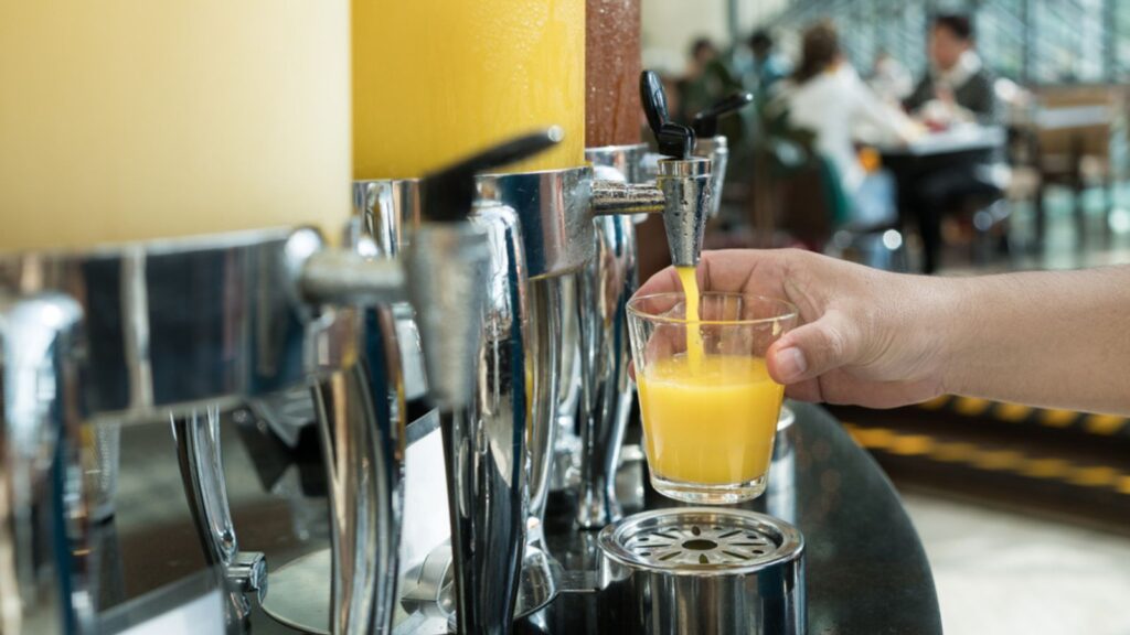 Hand holding glass refill orange juice for row of fresh juice at buffet
