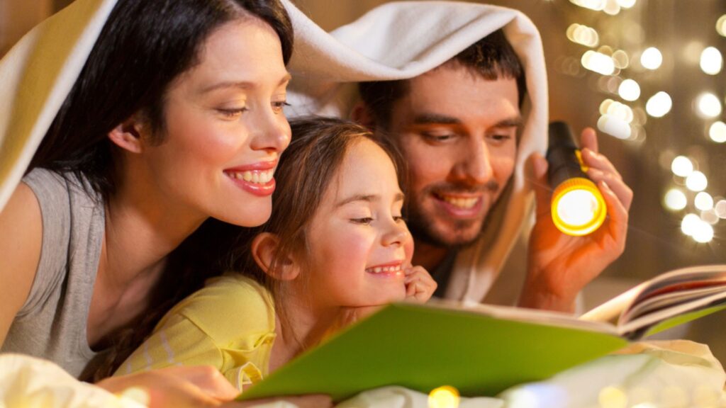Happy family reading book in bed at night at home