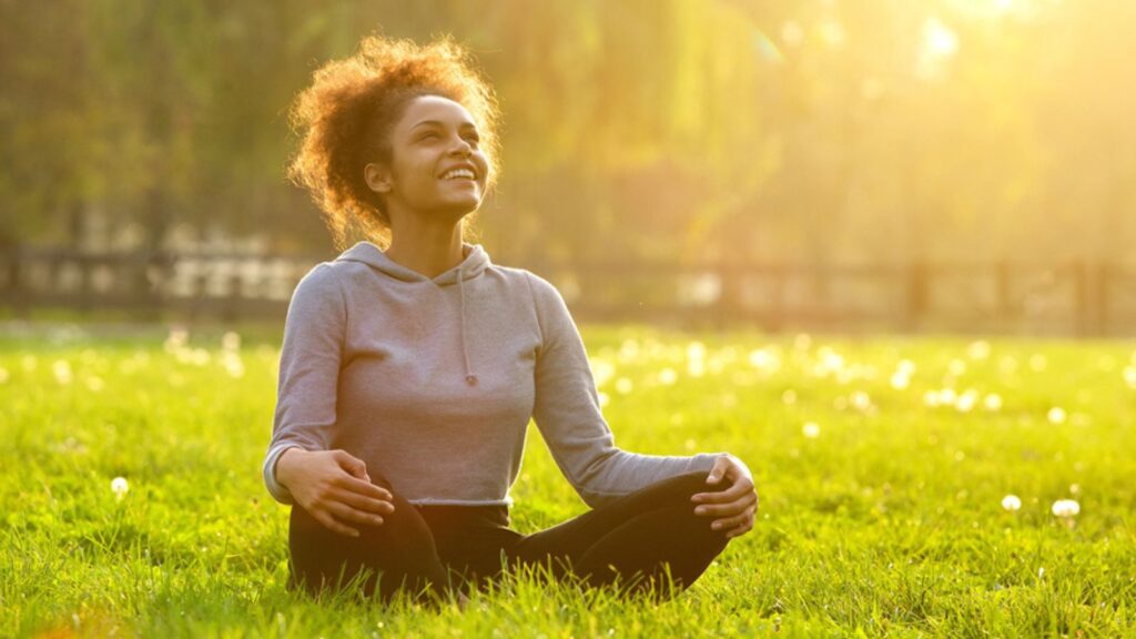 Happy young woman sitting in yoga position outside
