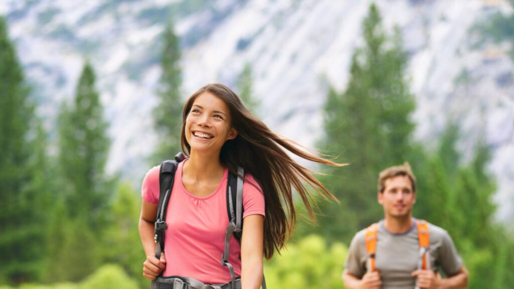 Hiking people walking on mountain trail landscape. Happy hikers h in outdoor nature looking up on green pine trees forest