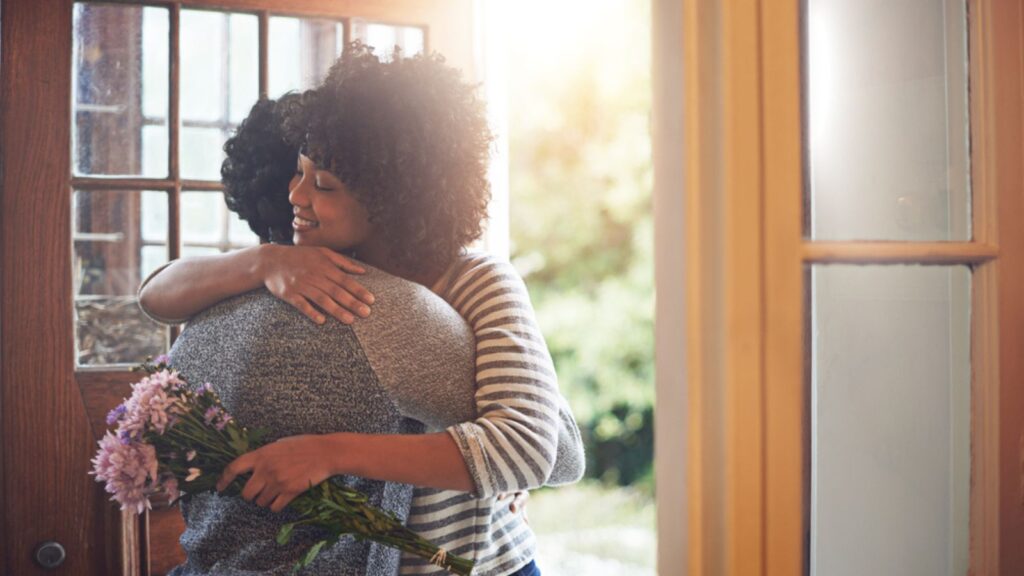 Love, hug and couple with flowers, gift and happiness with romance, bonding and anniversary. Partners, man or happy woman embrace, floral present