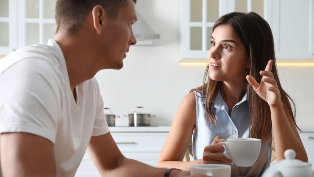 Man and woman talking while drinking tea at table in kitchen