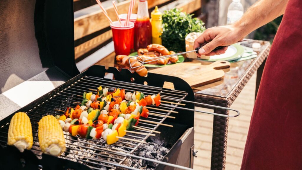 Man checking vegetables and sausages grilled for outdoors barbecue