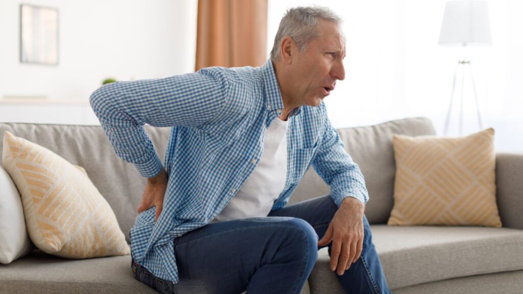 Mature man with side back pain sitting on couch at home