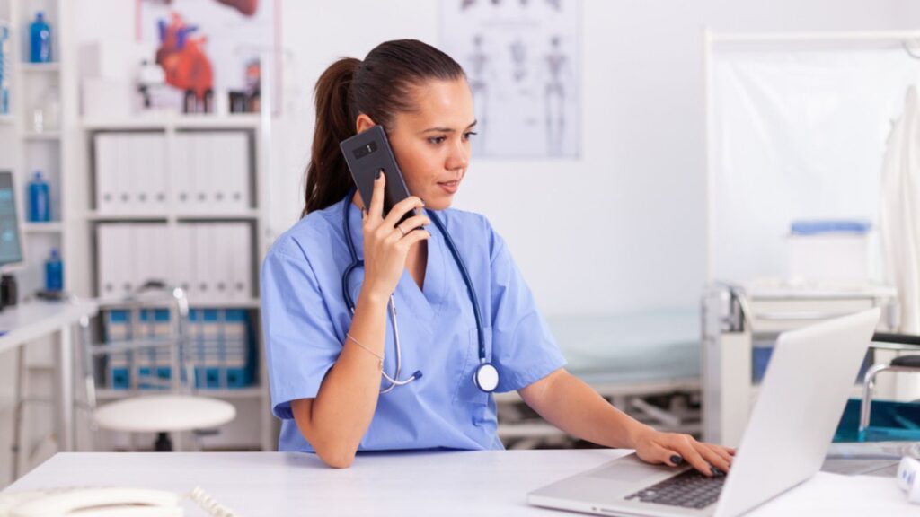 Medical practitioner using telephone and laptop