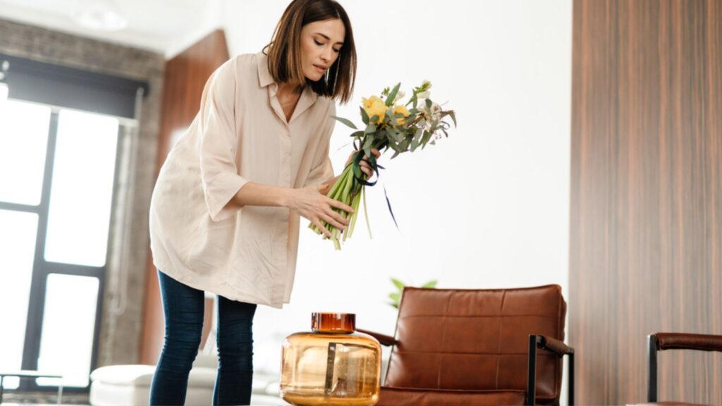 Middle aged woman decorating living room with flower bouquet in a vase