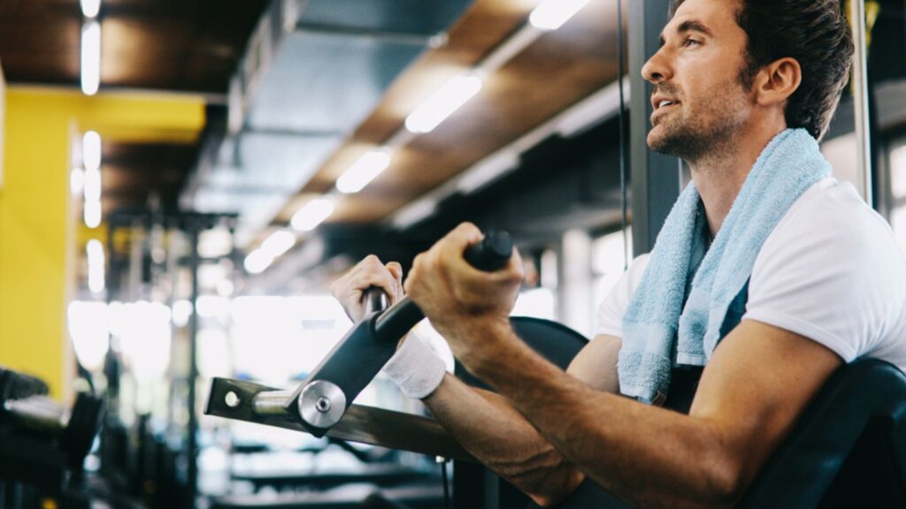 Muscular fit man working out in gym doing exercises with dumbbells at biceps