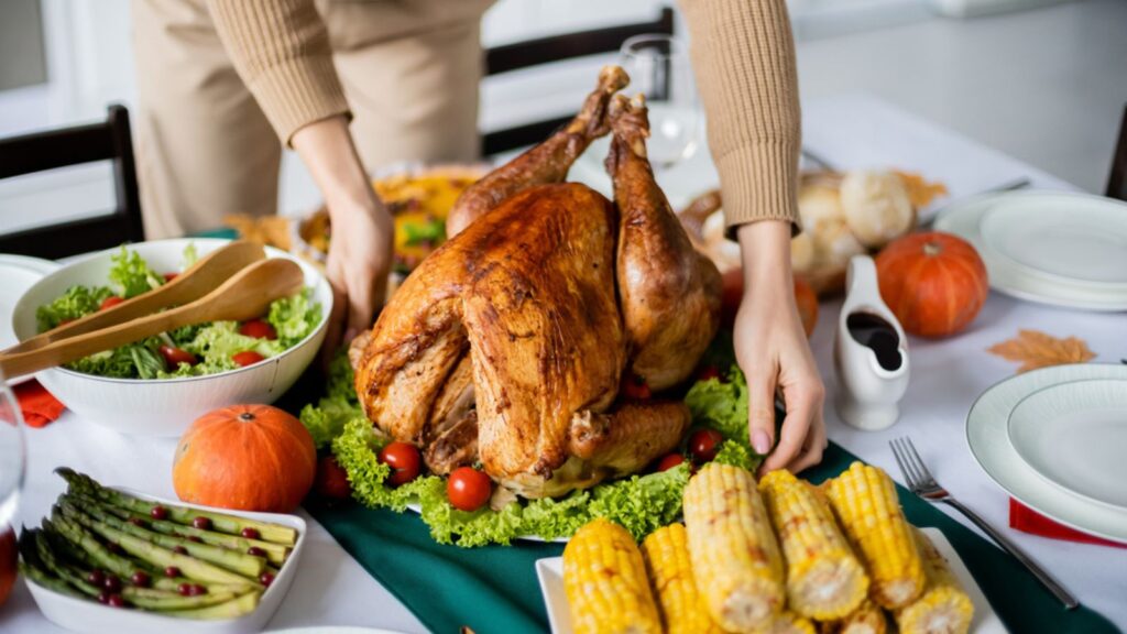 Partial view of woman serving traditional turkey near grilled corn and vegetable salad for thanksgiving dinner