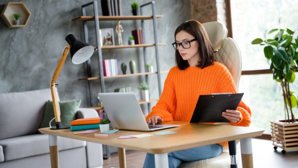 Photo of serious busy woman dressed orange pullover checking working on her laptop at home