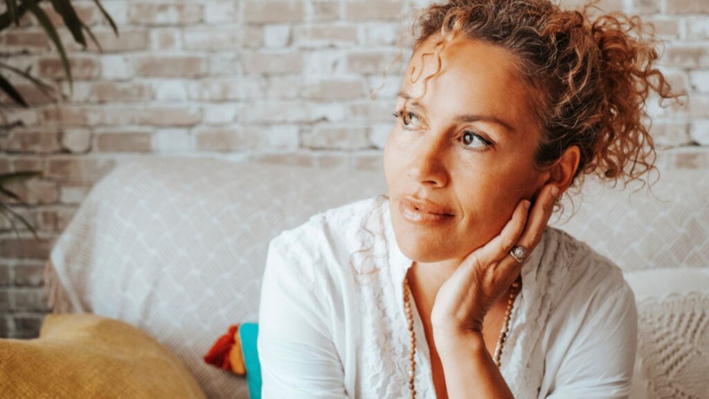Portrait of serene woman looking outside the window at home having relax time sitting on the couch. Attractive middle age thinking happy indoor