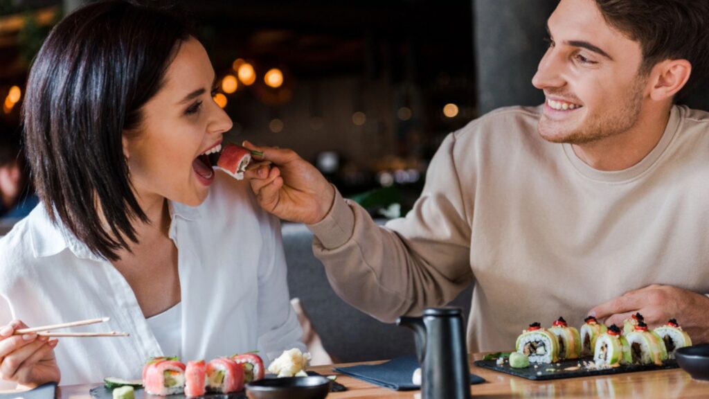 Selective focus of happy man holding chopsticks with tasty sushi near young woman in restaurant
