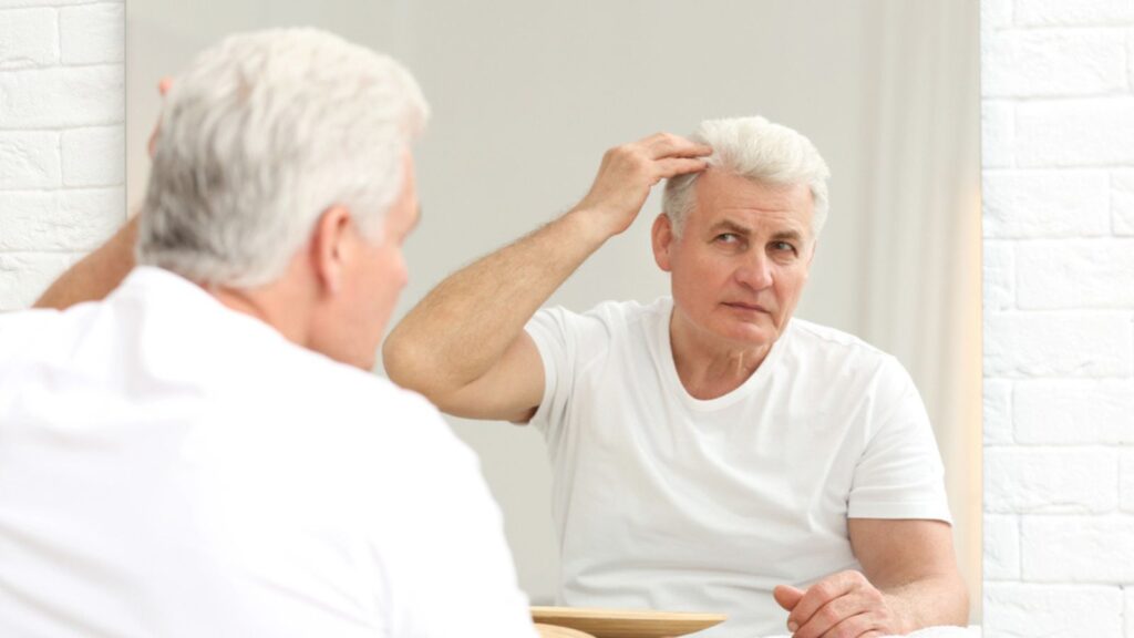 Senior man with hair loss problem looking in mirror indoors