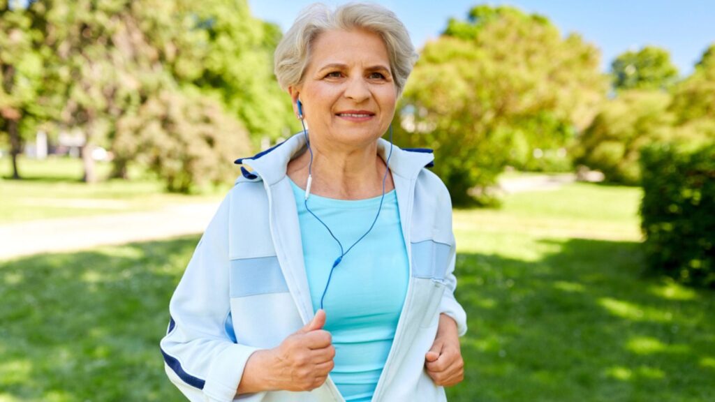 Senior woman with earphones running in summer park