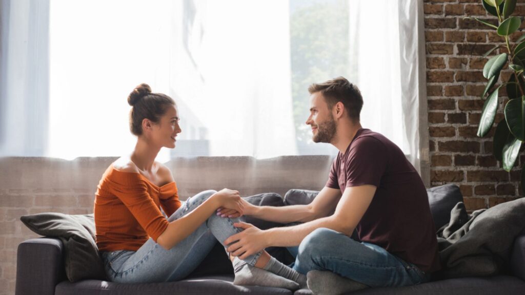 Side view of young couple talking while sitting on sofa and holding hands