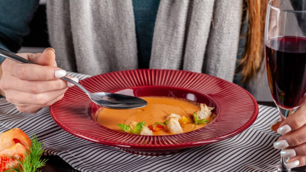 The concept of Spanish cuisine. The girl in the restaurant has gazpacho soup and drinks red wine. Squeezes lemon in the soup