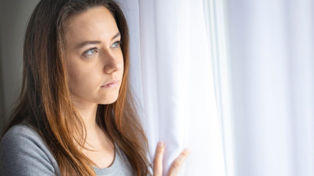 Thinking and stressed woman looking through a window