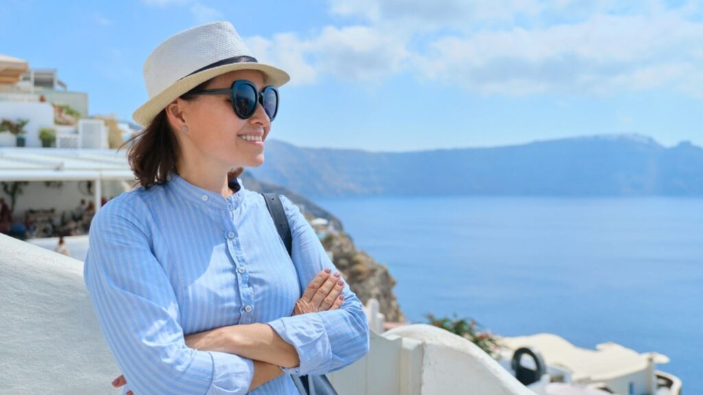 Tourist business, confident businesswoman, owner with folded arms posing background of landscape of Oia village Santorini island, copy space