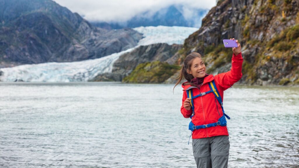 Tourist woman taking selfie photo at Mendenhall glacier in Juneau, Alaska. Famous tourism destination on Alaska cruise, USA travel