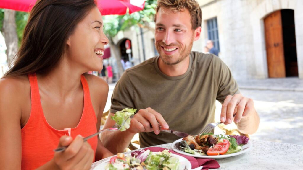 Tourists couple eating salad at outdoor cafe