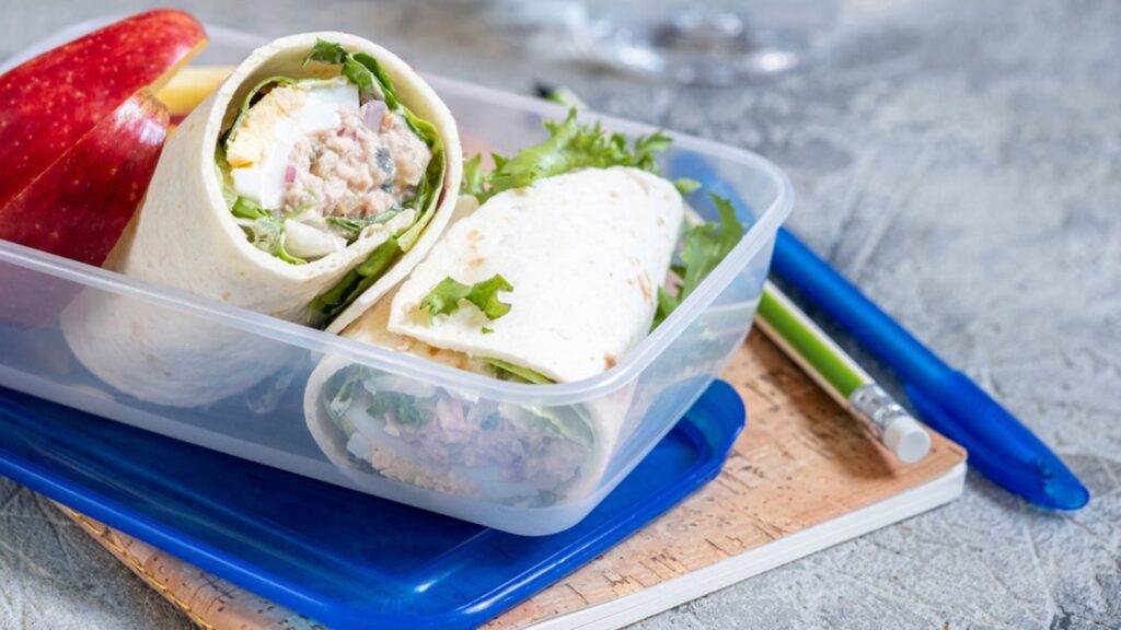 Tuna salad wraps in lunch box with apple